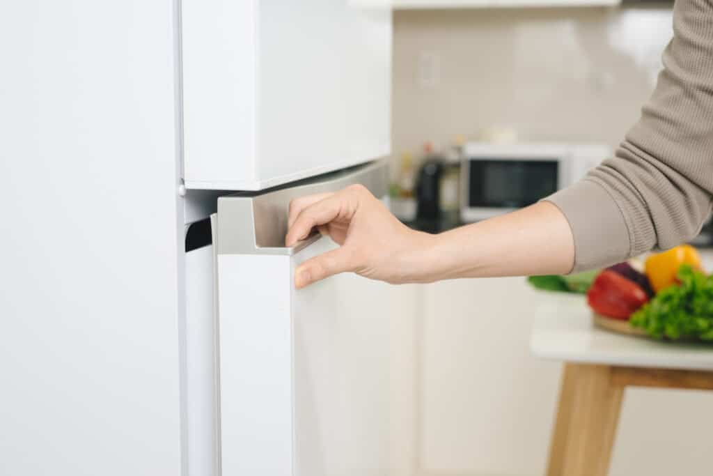 Male hand is opening white refrigerator door